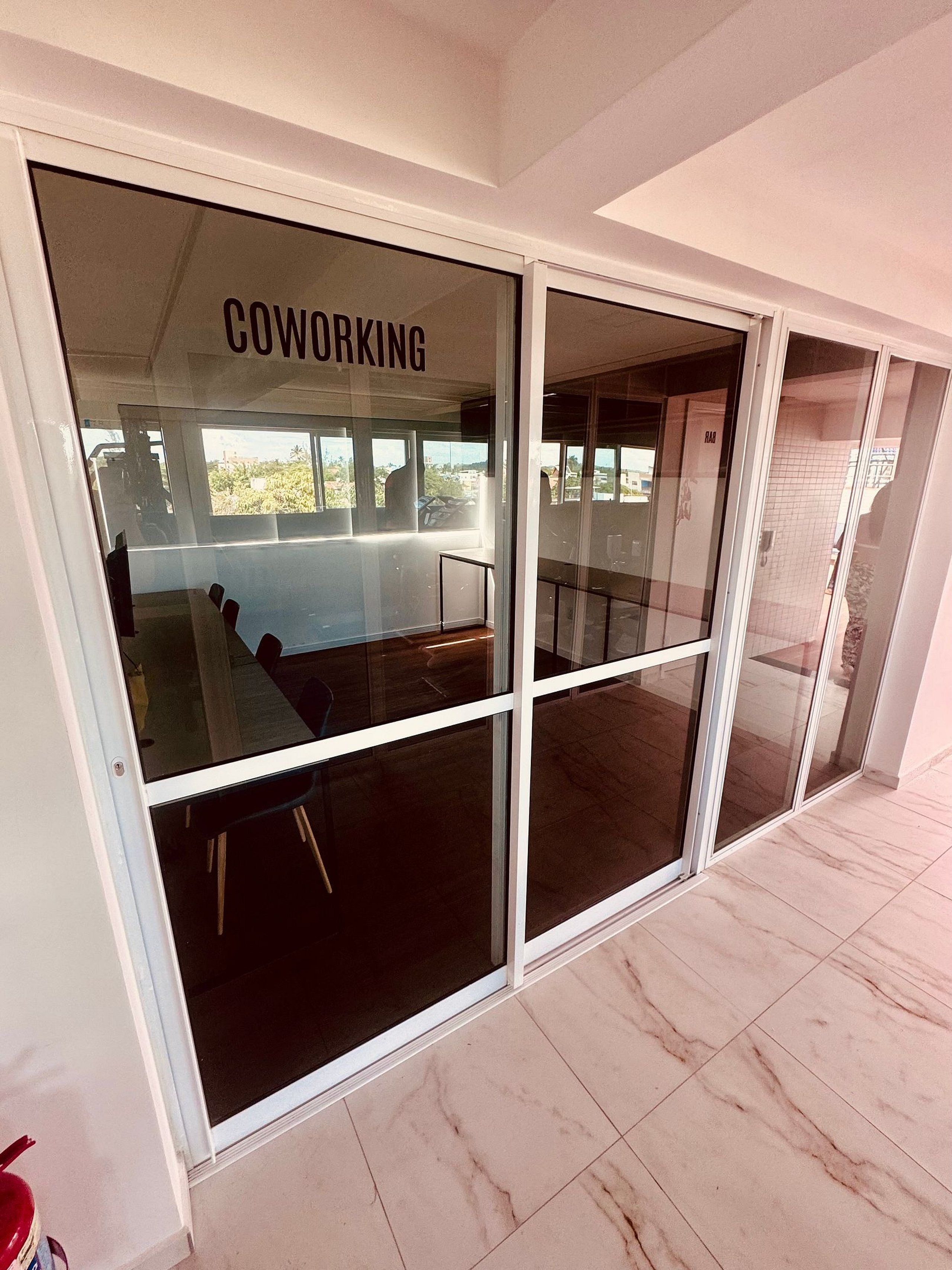 Uma porta de vidro com a palavra 'COWORKING' escrita, que dá acesso a um espaço interior com varanda.
