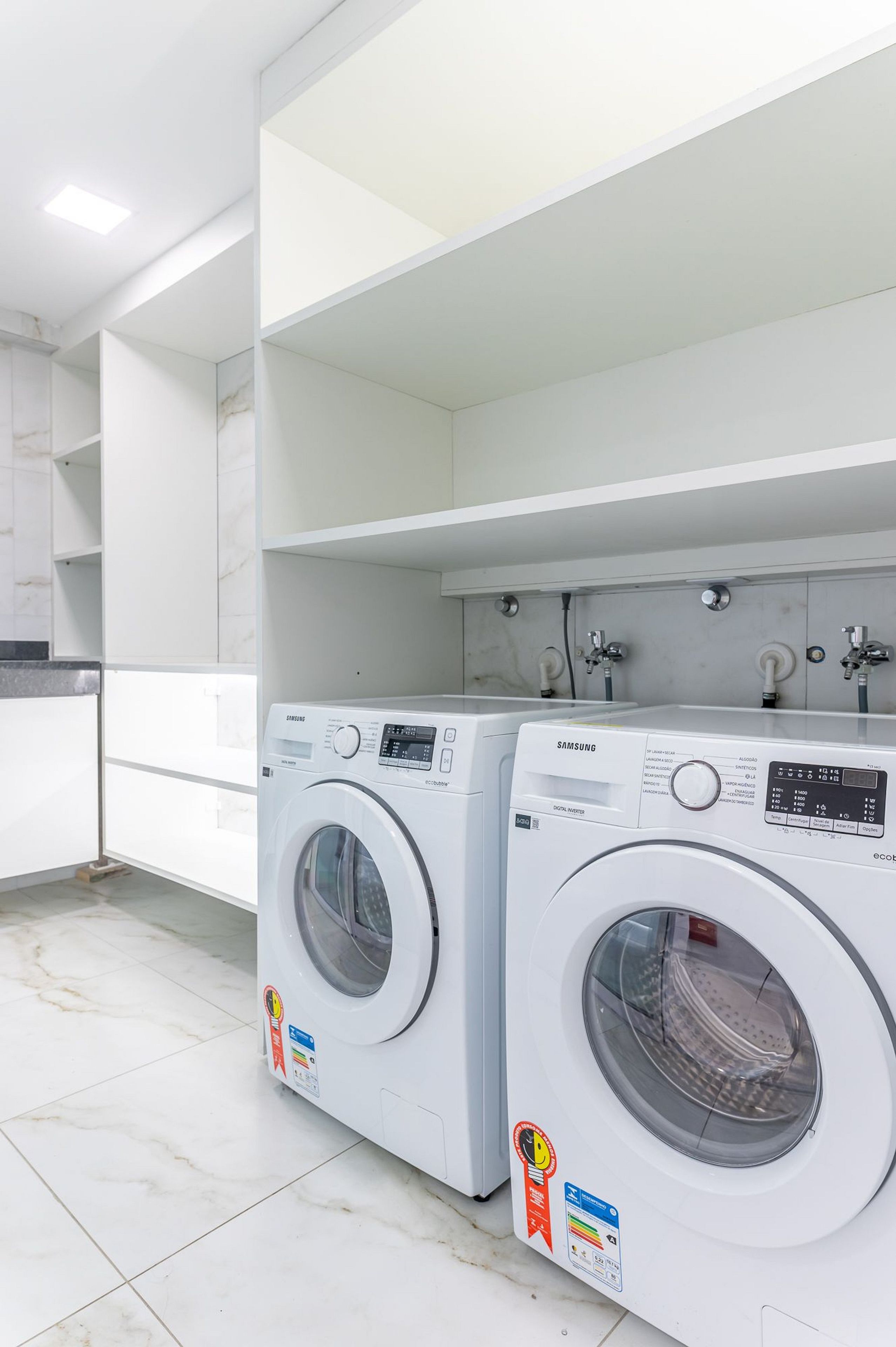 Una sala de lavandería con dos lavadoras Samsung, piso de baldosas y paredes blancas.