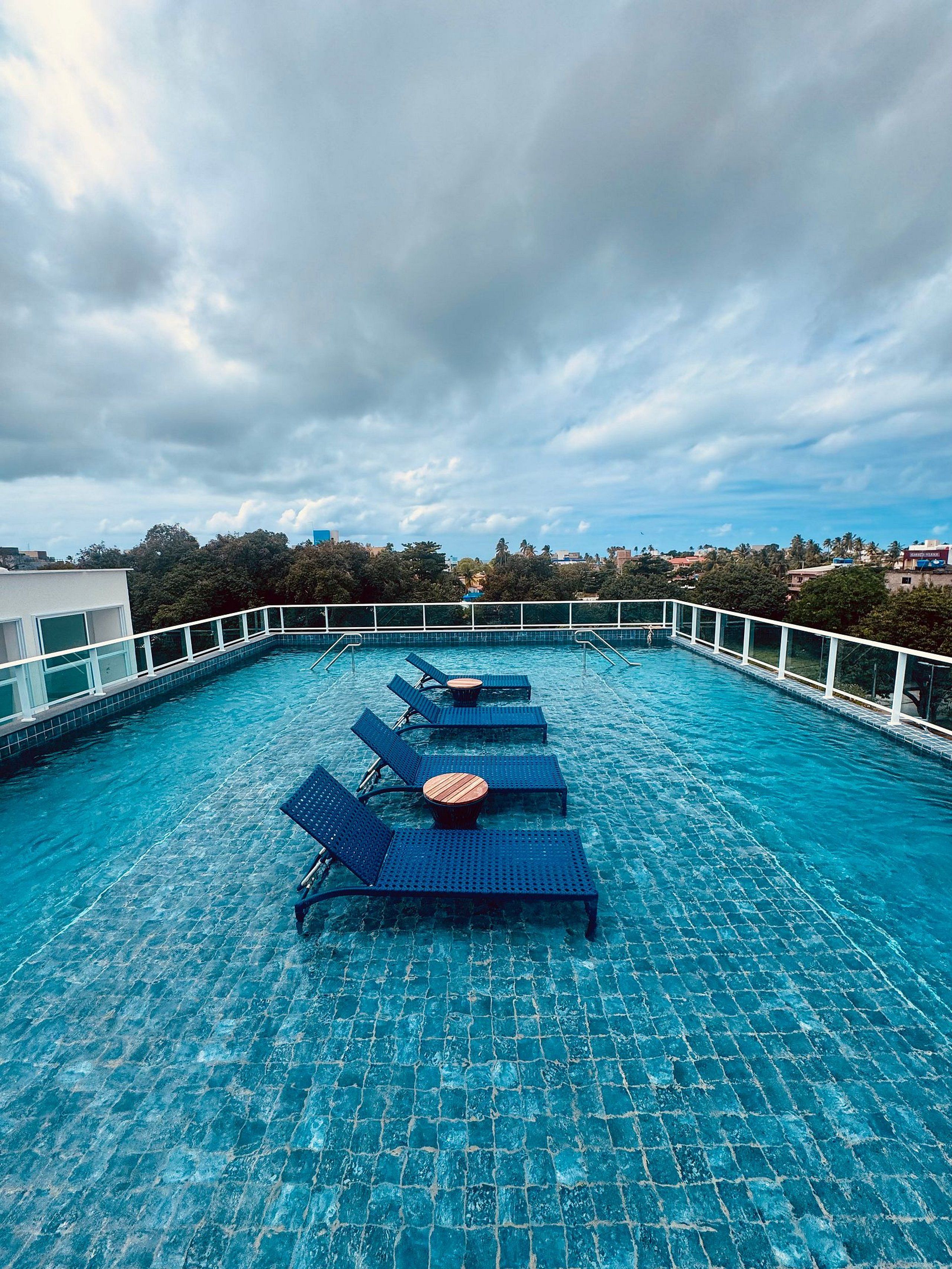 Una piscina sul tetto con sedie a sdraio blu e ringhiera in vetro.