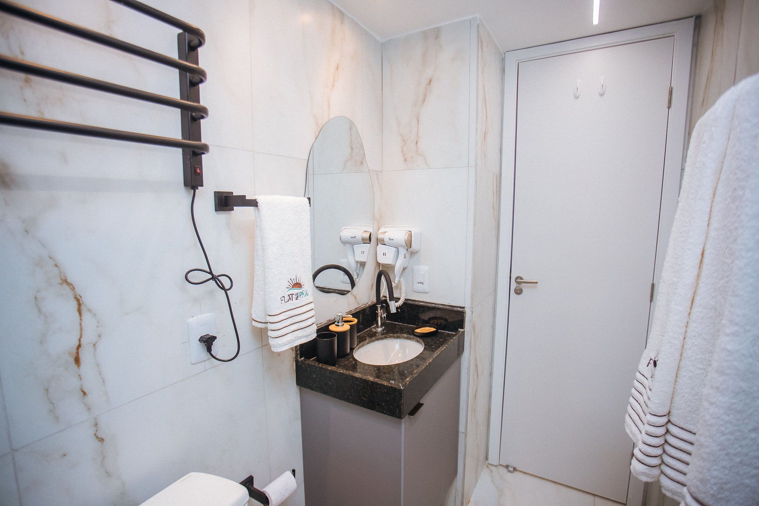 A bathroom with a marble wall, a sink with a black countertop, a towel rack, a mirror, and a white door.