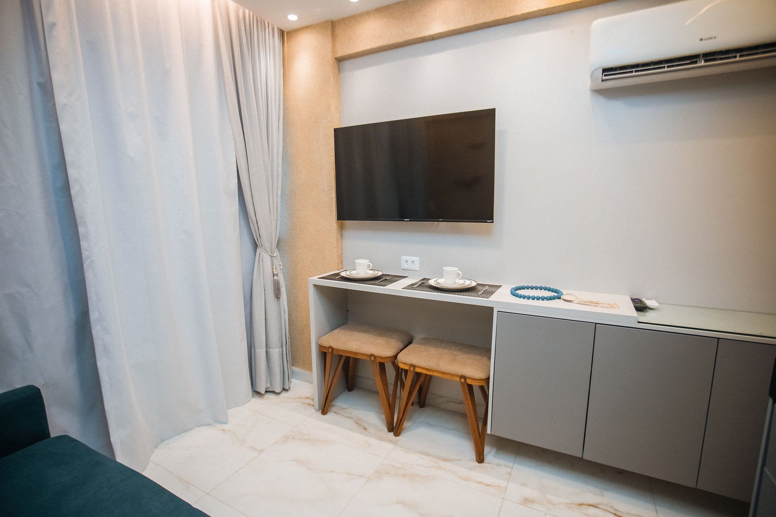 Una habitación moderna con escritorio, dos sillas, un televisor de pantalla plana y un equipo de aire acondicionado.