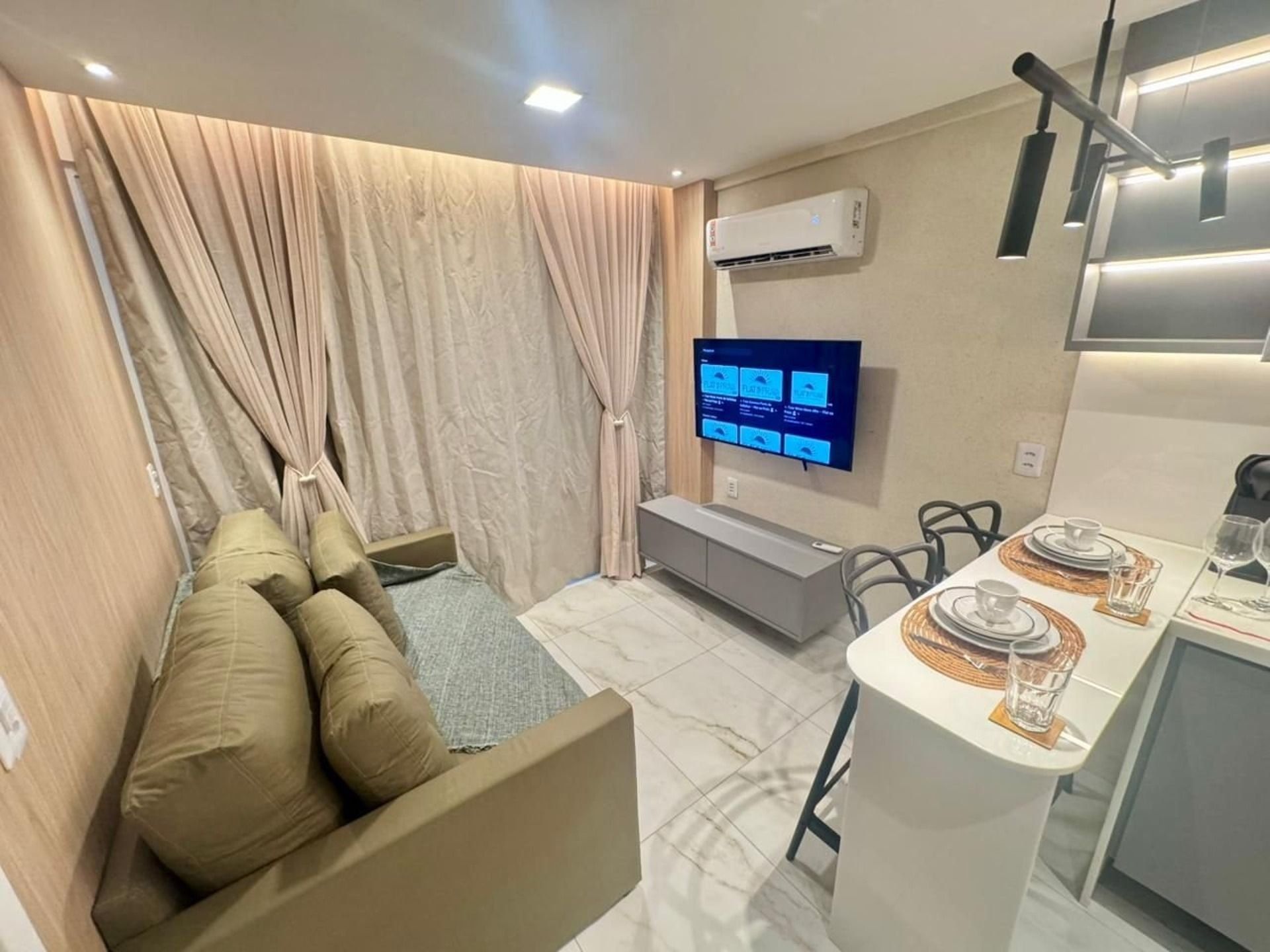 A modern living room with a sofa, a flat-screen TV, and a dining area with a table set for two.