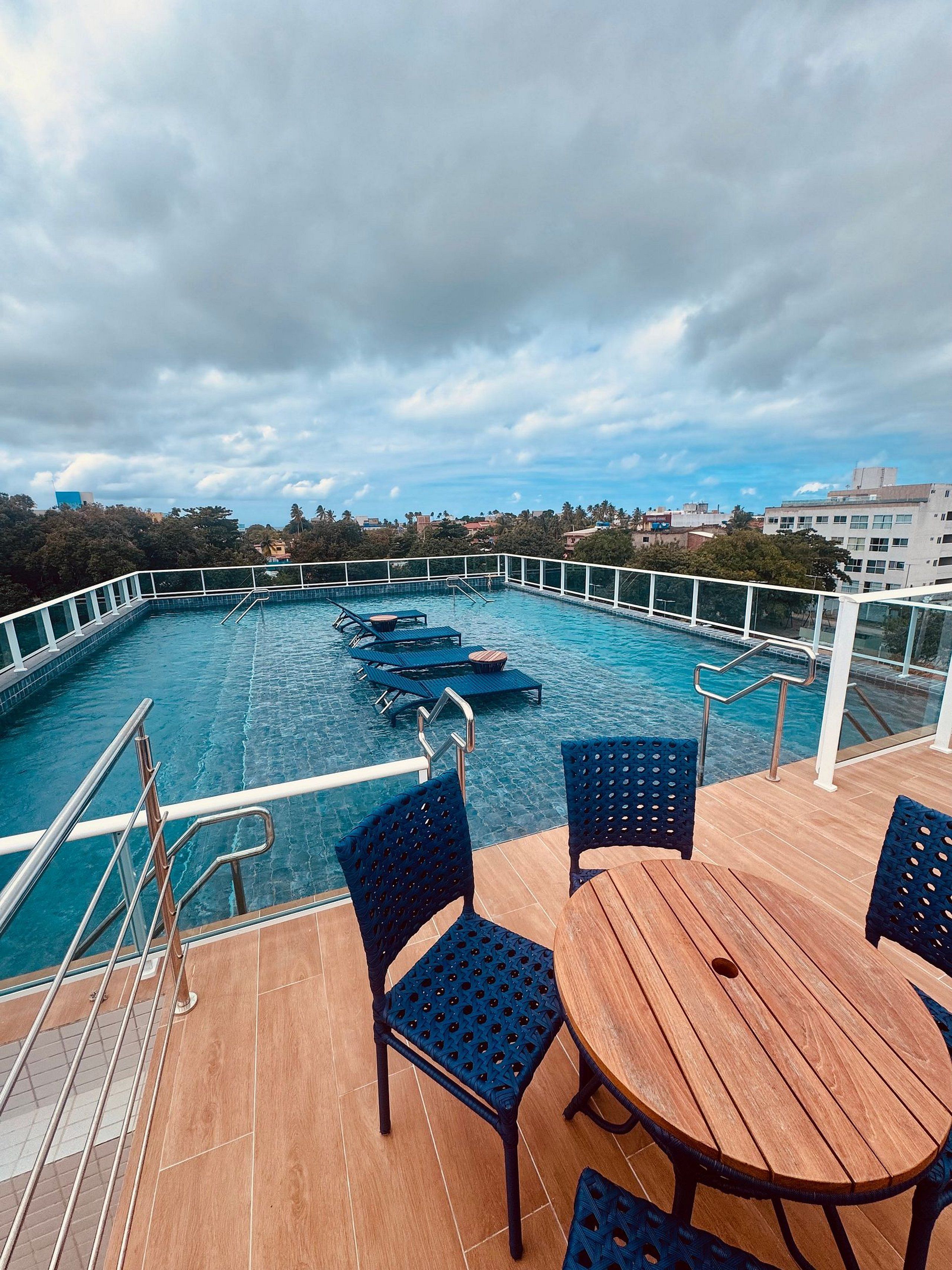 Una piscina en la azotea con vistas a la ciudad, que incluye una mesa de madera y sillas azules.