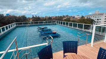 Una piscina en la azotea con vistas a la ciudad, que incluye una mesa de madera y sillas azules.