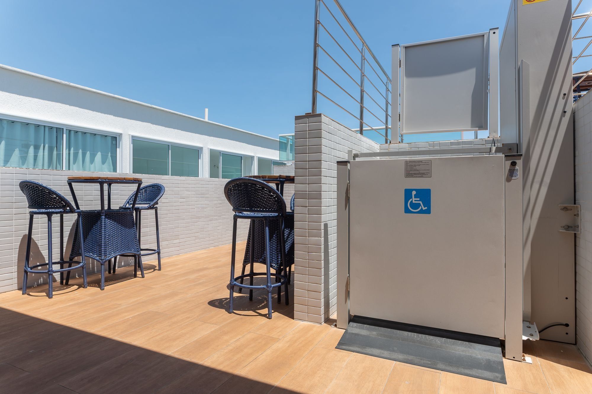 Una terraza con dos sillones de mimbre, una mesita y un refrigerador con el símbolo de accesibilidad para sillas de ruedas.
