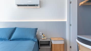Un dormitorio con cama, aire acondicionado, mesita de noche, una pequeña mesa, un cesto de basura y un armario.