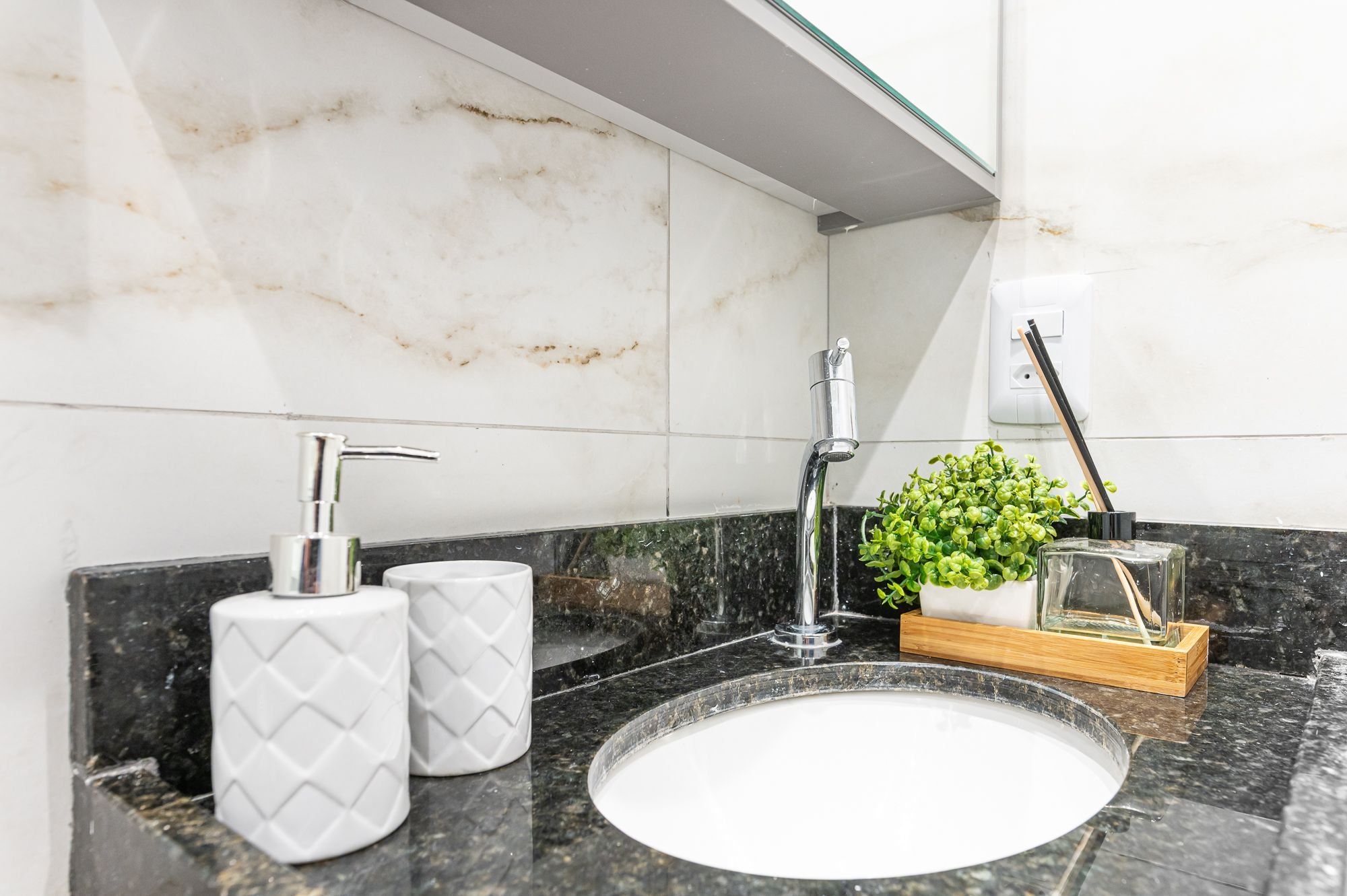 Une salle de bain avec un lavabo en marbre, un robinet moderne et une petite plante en pot.