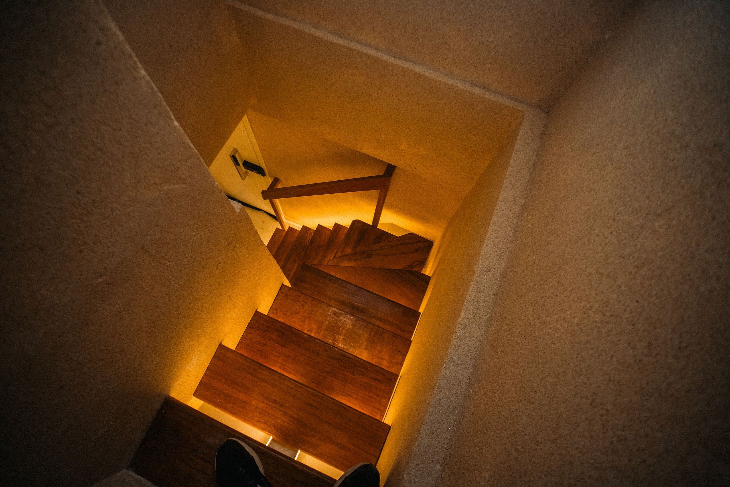 Un escalier en bois, doté d’une main courante, qui monte dans un espace étroit.