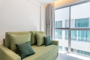 A modern living room with a sofa and pillows, large windows, and a view of buildings.