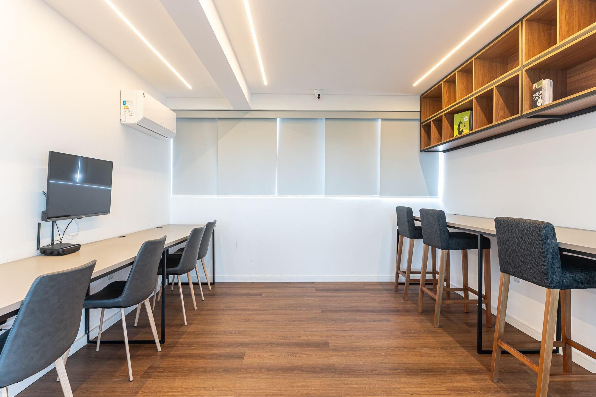Une salle de réunion moderne équipée d’une longue table, de chaises, d’un téléviseur à écran plat et d’une bibliothèque en bois.