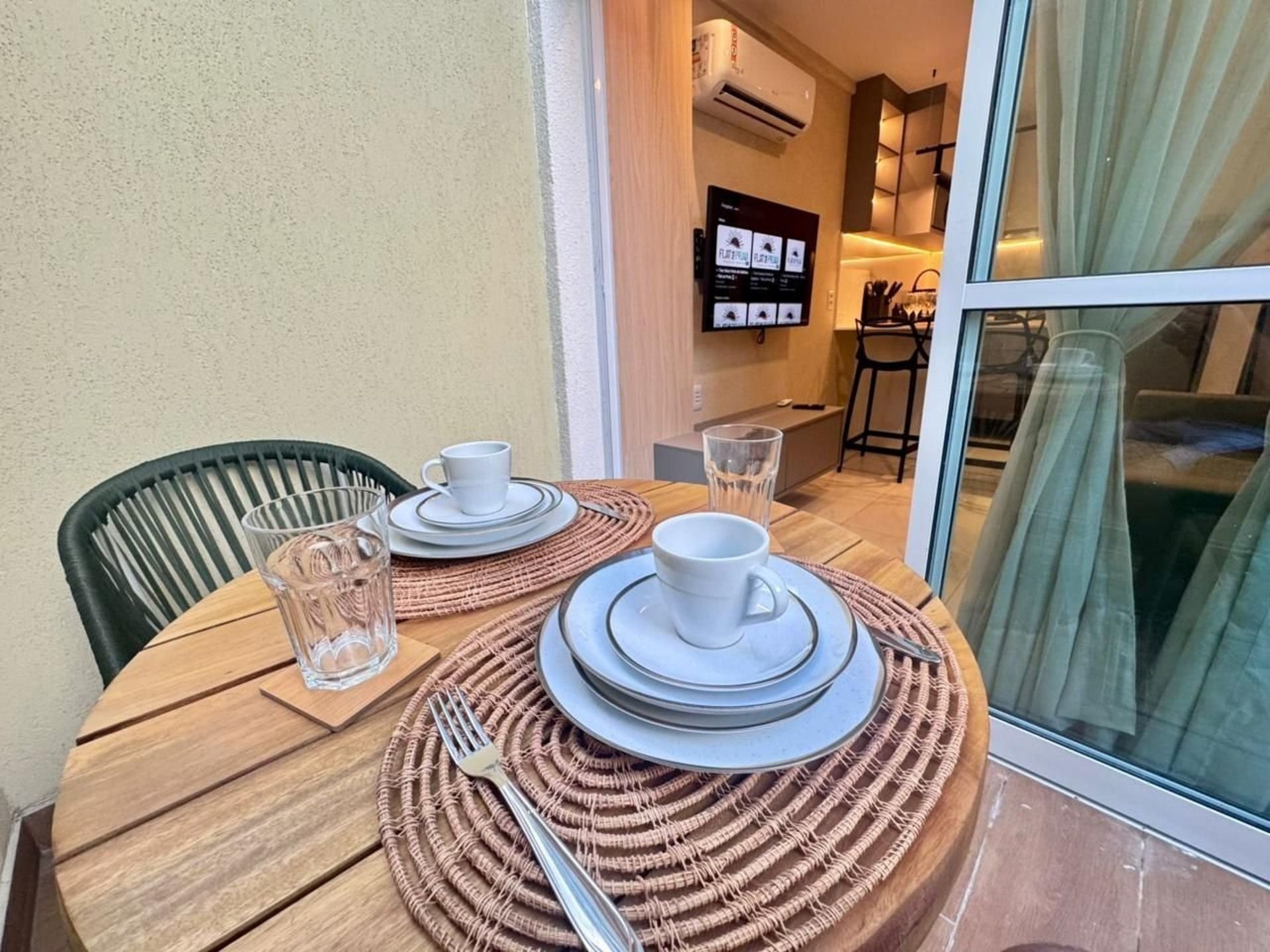 Mesa de jantar posta com pratos, copos e talheres, acompanhada de uma cadeira e um copo de água.