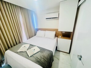 A hotel room with a bed, a bedside table, a wardrobe, and a window with curtains.
