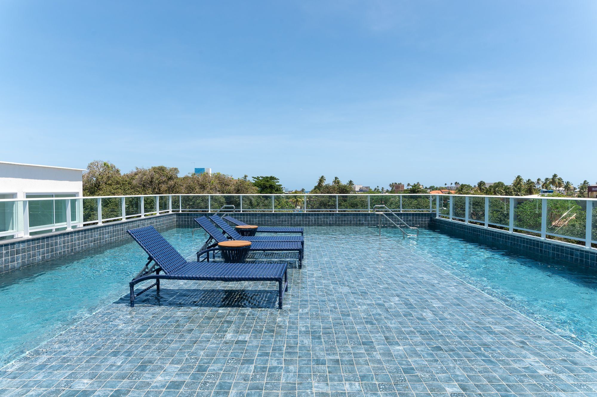 A rooftop pool with blue lounge chairs and a clear view of the city skyline.
