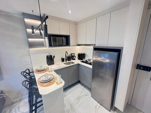 A compact kitchen with modern appliances, a microwave, and a stainless steel refrigerator. - Essenza Porto de Galinhas - Flat na Praia (Ipojuca)