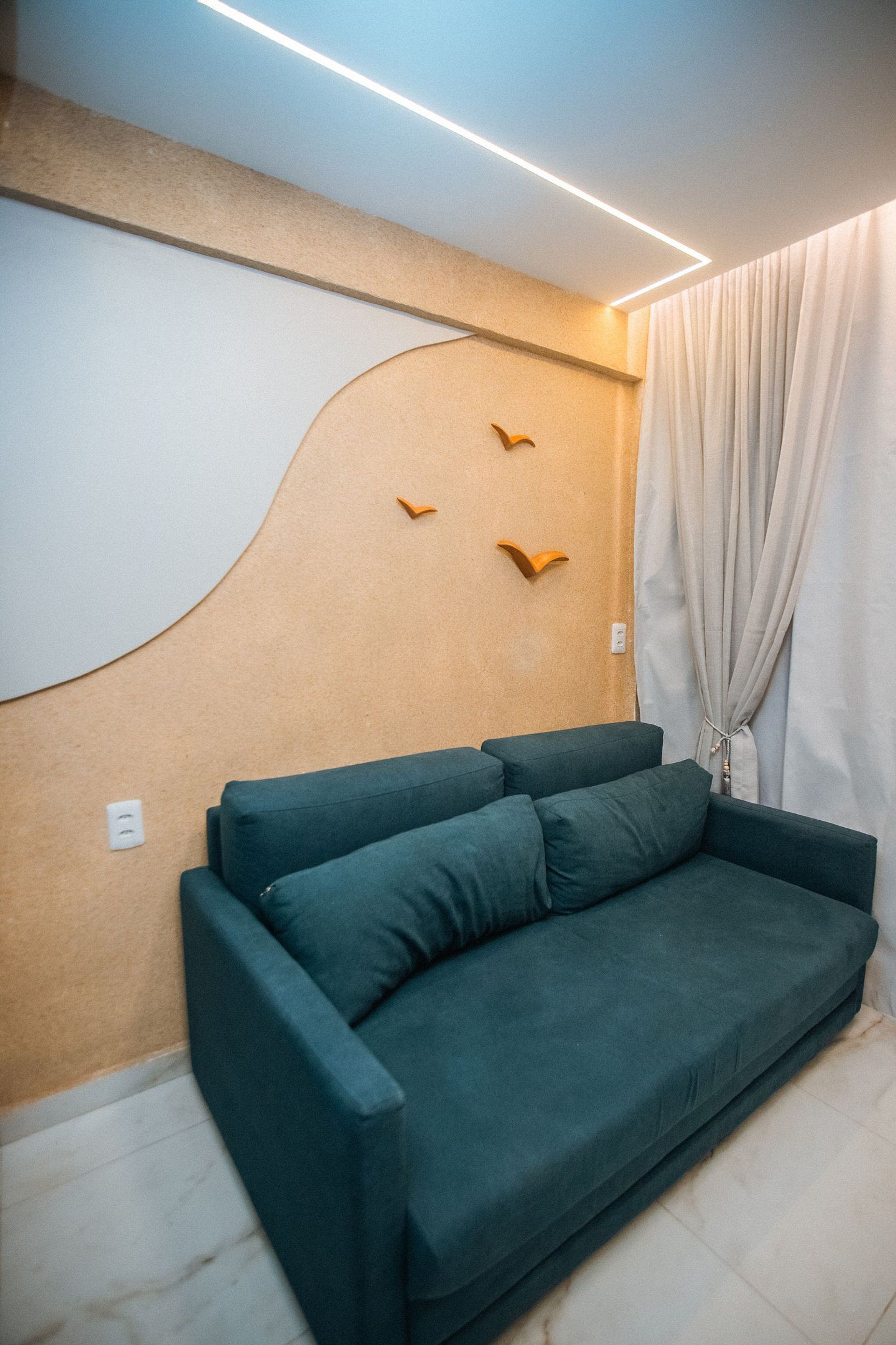A modern living room with a green sofa, a wall-mounted light fixture, and a curtain.