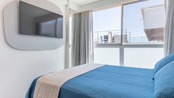 Quarto de hotel com cama, televisão montada e uma janela grande com vista para o exterior.