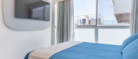 A hotel room with a bed, a mounted TV, and a large window with a view of the outside.