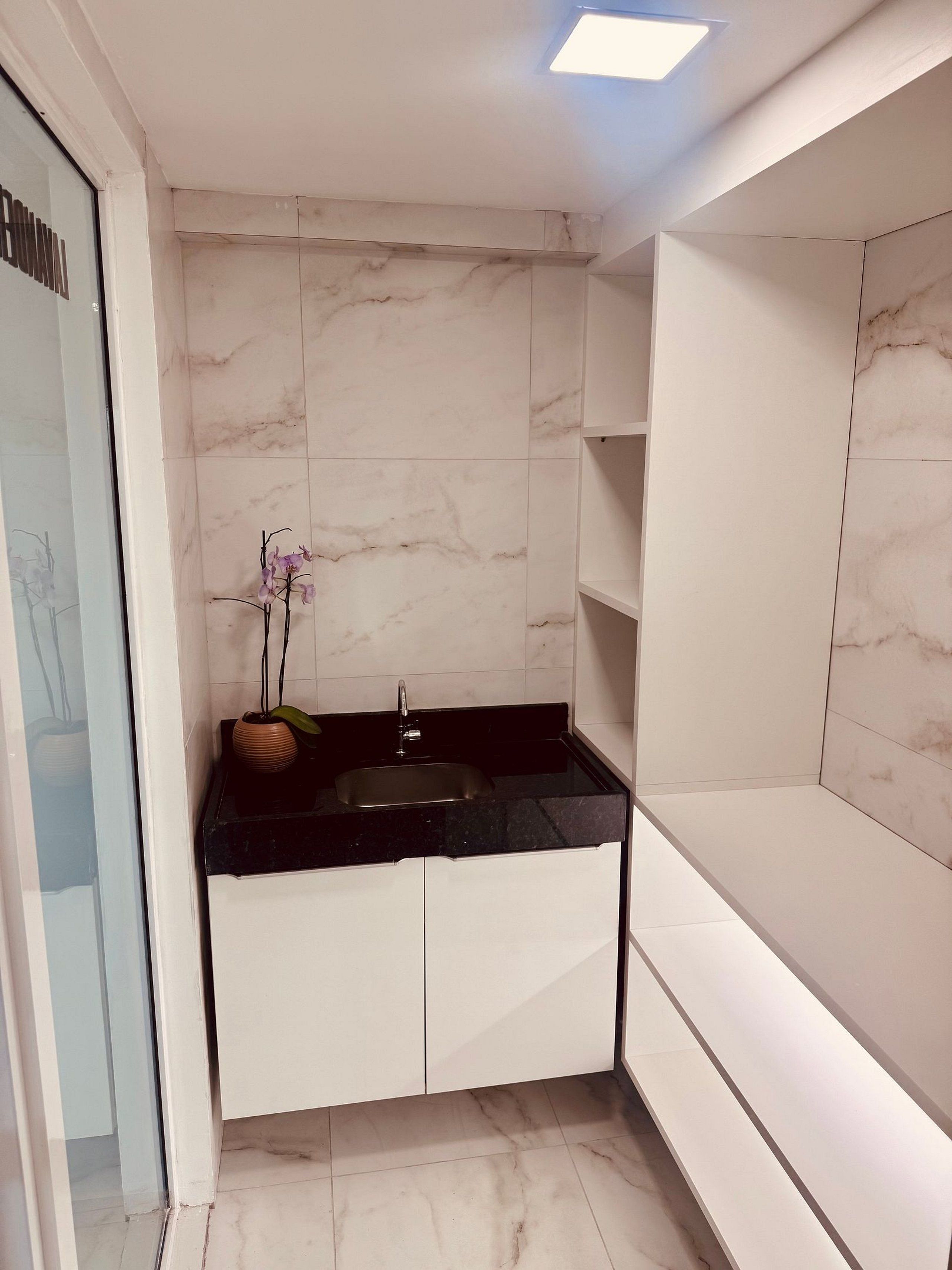 Cozinha moderna com ladrilhos de mármore, bancada preta, pia e uma orquídea em vaso.