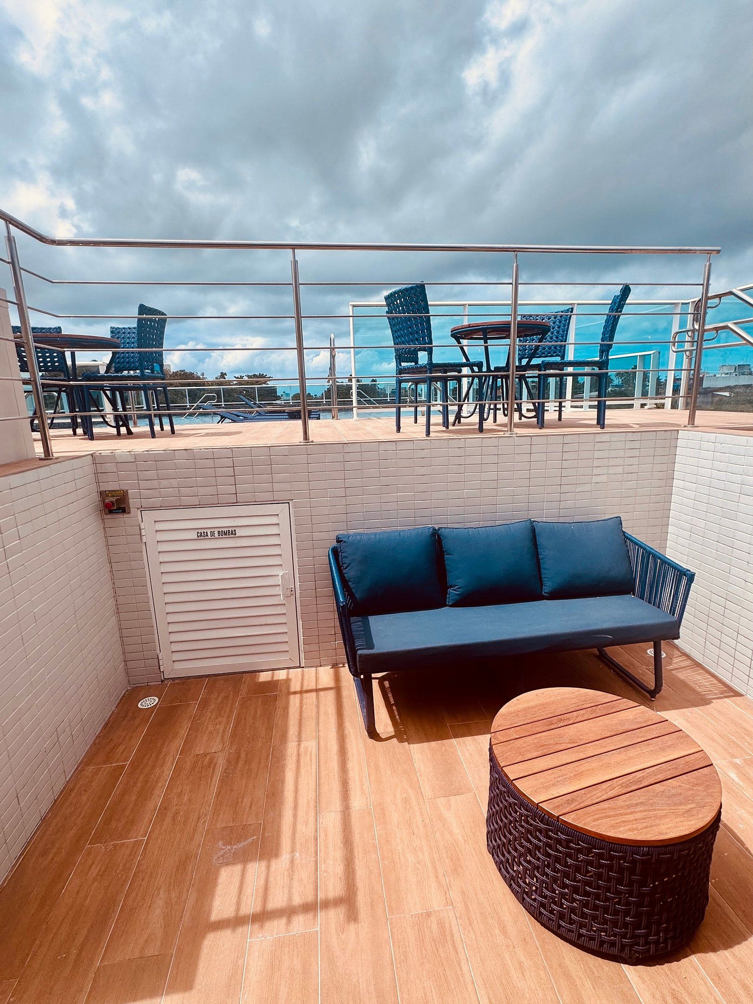 Terraço no telhado com um sofá azul, mesa de vime e cadeiras azuis.