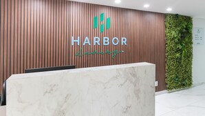 Una reception con un pannello di legno a parete, un logo con 'HARBOR' e 'Luzurg' e una parete verde con piante.