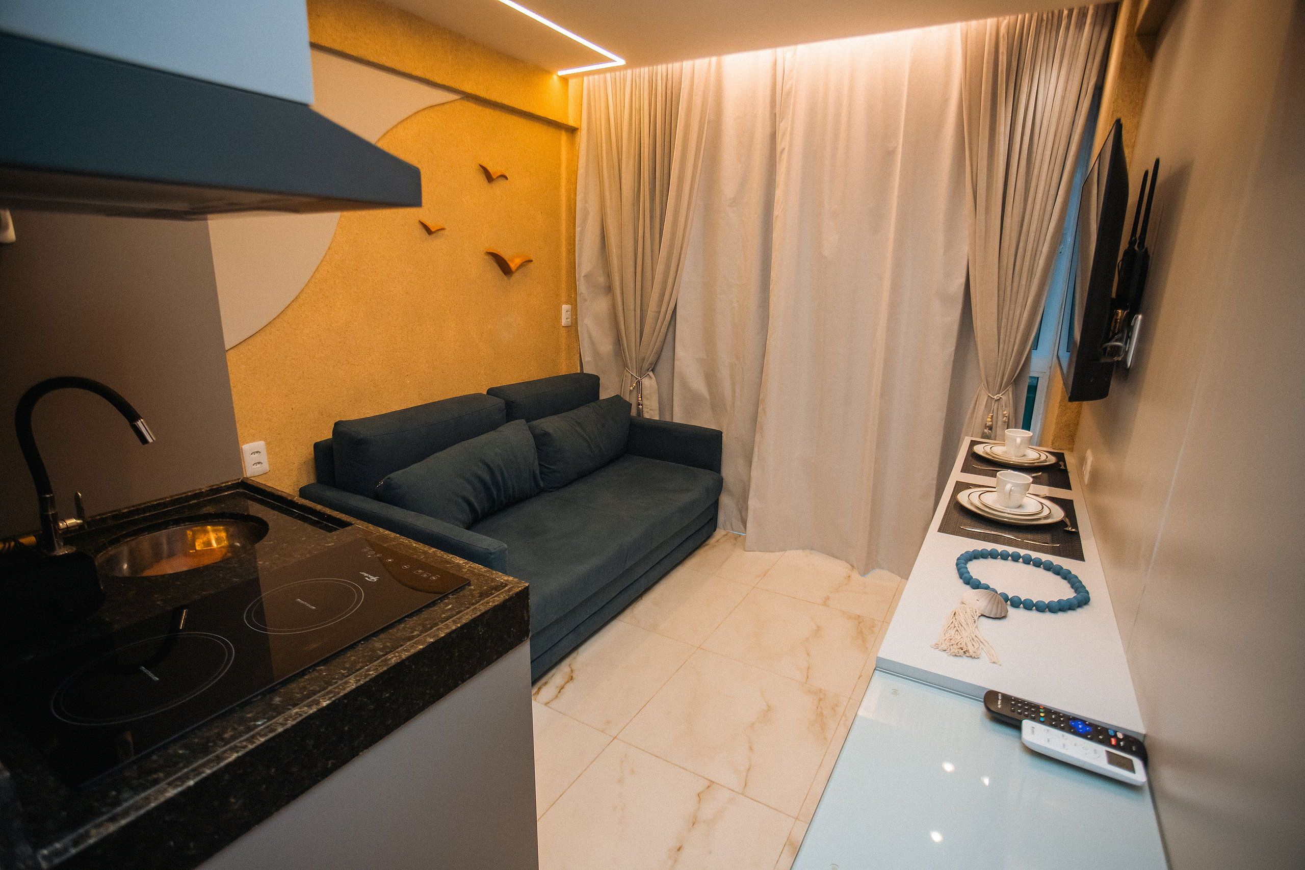 A compact kitchenette with a stove, a sofa, and a dining area with a remote control.