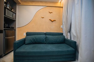 Um sofá azul-turquesa com duas almofadas, uma área de cozinha com eletrodomésticos e uma parede com design exclusivo.