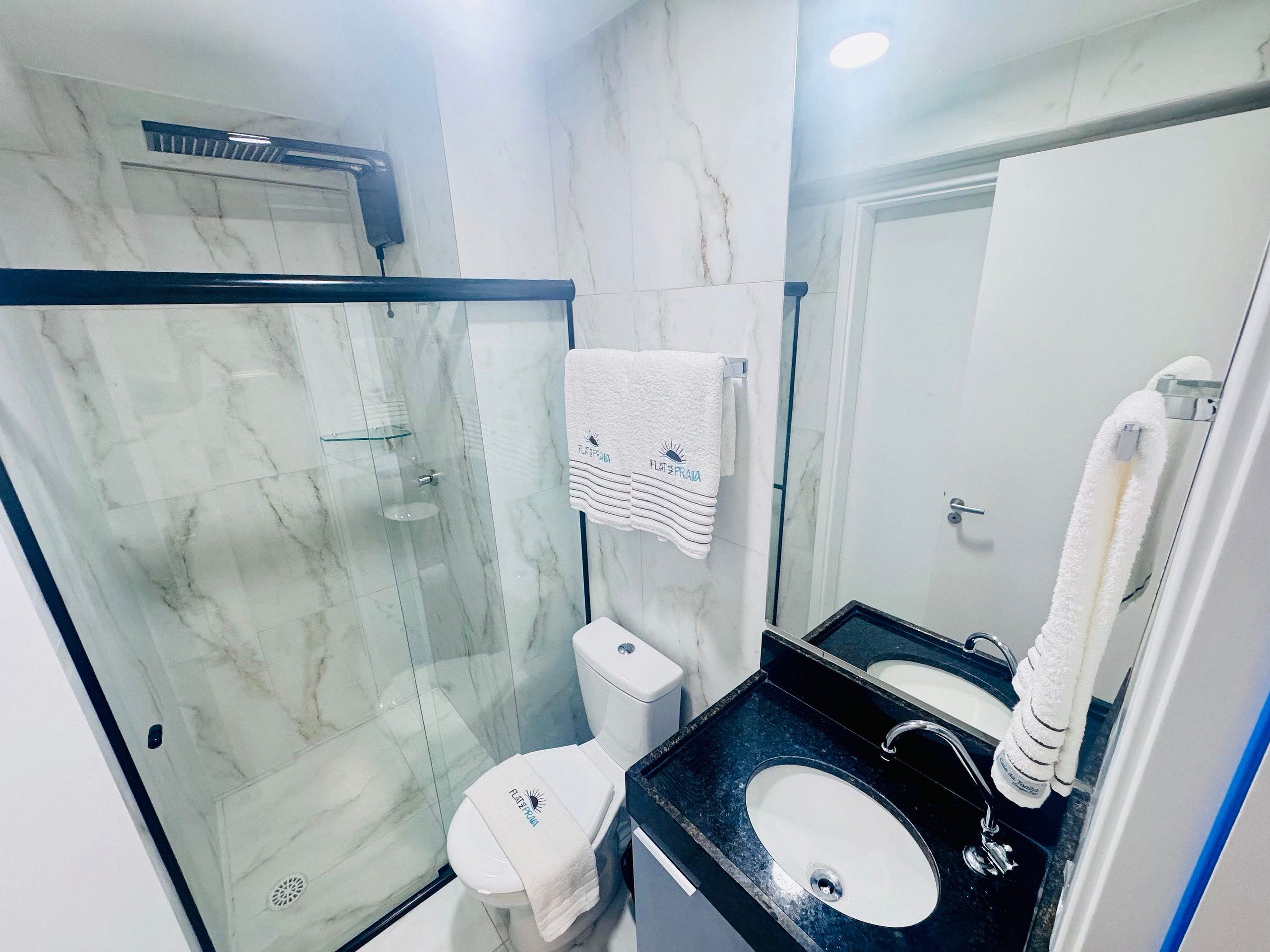 A modern bathroom with a glass-enclosed shower, a toilet, a sink, and a mirror.