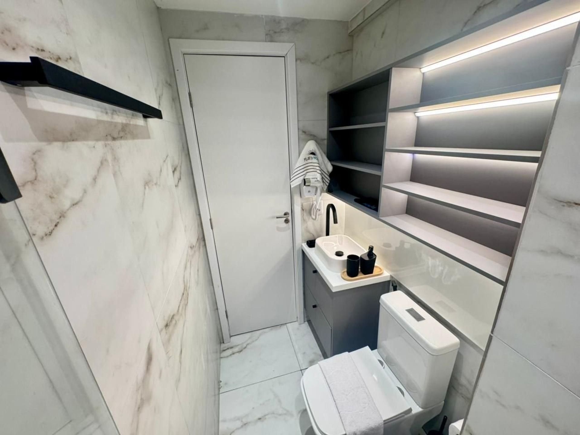 A compact bathroom with a white door, a sink with a towel, and a toilet.