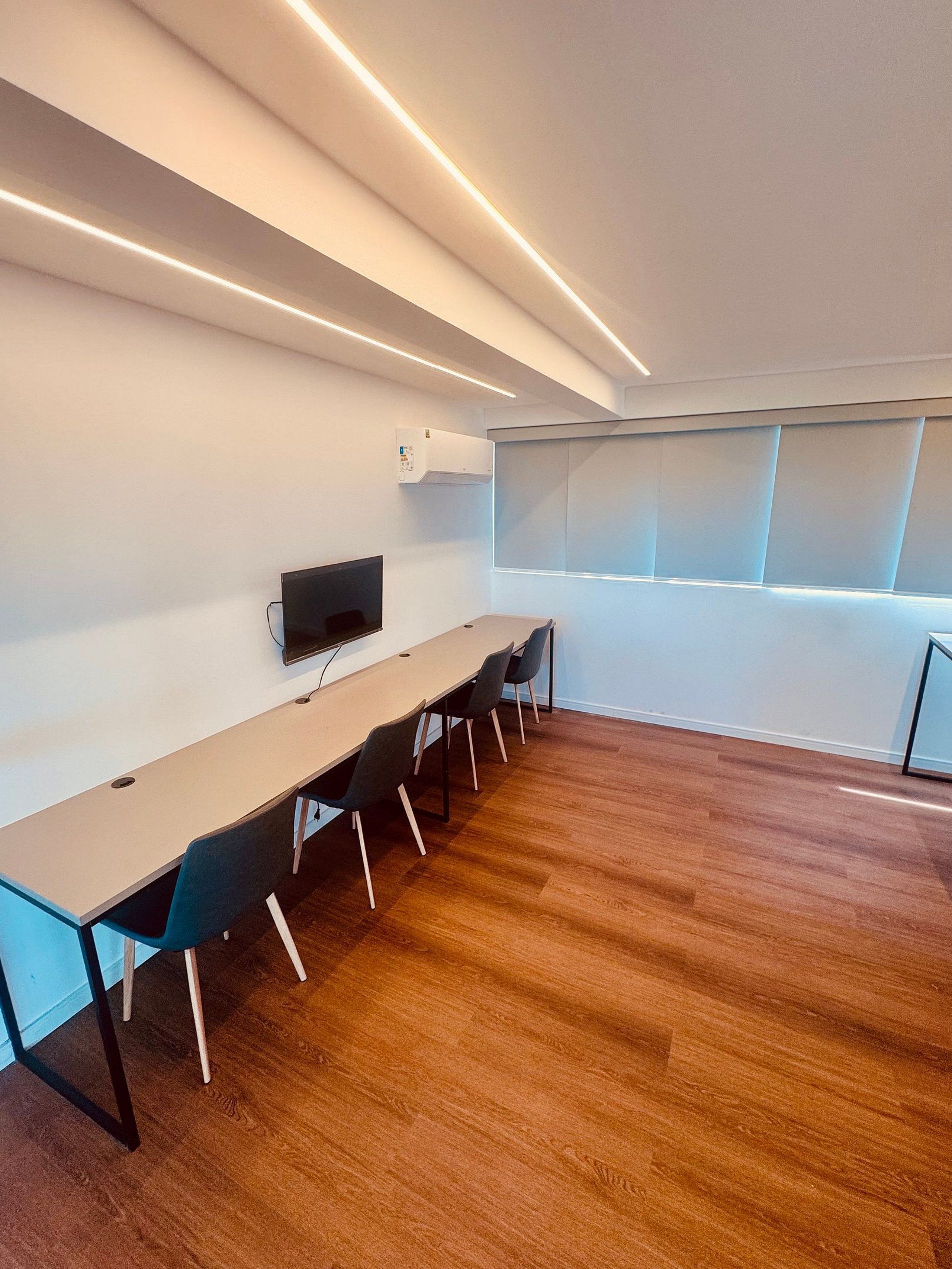A conference room with a long table, chairs, a flat-screen TV, and an air conditioning unit.