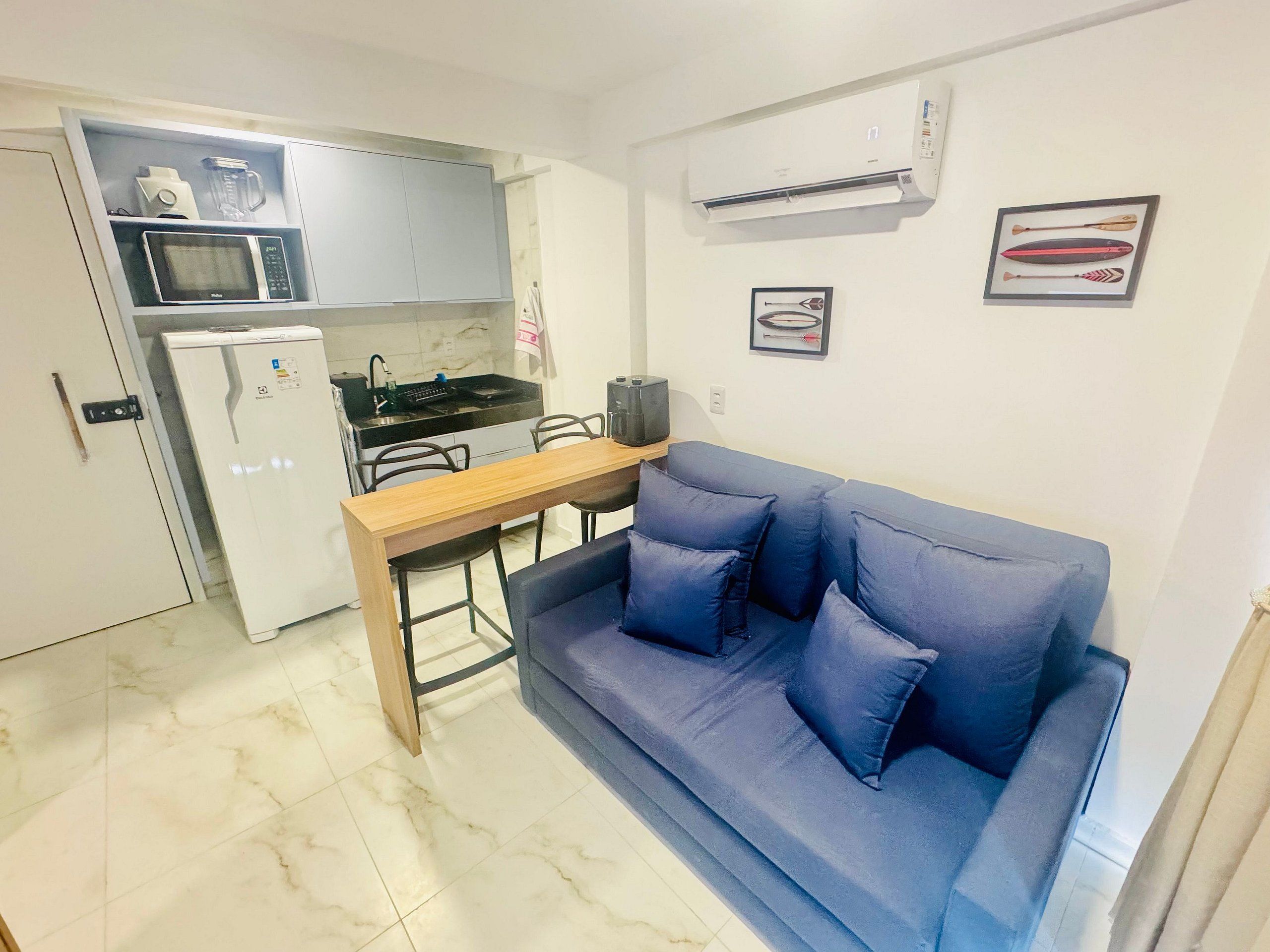 Un espacio habitable compacto con kitchenette, un sofá azul, una mesa de madera y un televisor.