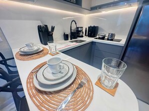 A modern kitchen with a dining area set for two, featuring a white table, stainless steel appliances, and a black faucet.