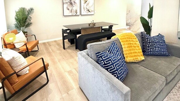 A modern living room with a grey sofa, a dining table, and two chairs. There are two wall-mounted paintings, a potted plant, and a bench. - Classy 4-bedroom house with AC in Redondo Beach (Redondo Beach)