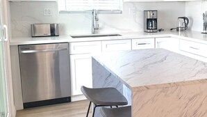 A modern kitchen with white cabinets, a stainless steel dishwasher, a coffee maker, and a marble countertop. - Classy 4-bedroom house with AC in Redondo Beach (Redondo Beach)