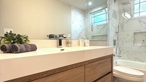 A modern bathroom with a marble backsplash, a wooden vanity, a toilet, and a shower area. - Classy 4-bedroom house with AC in Redondo Beach (Redondo Beach)