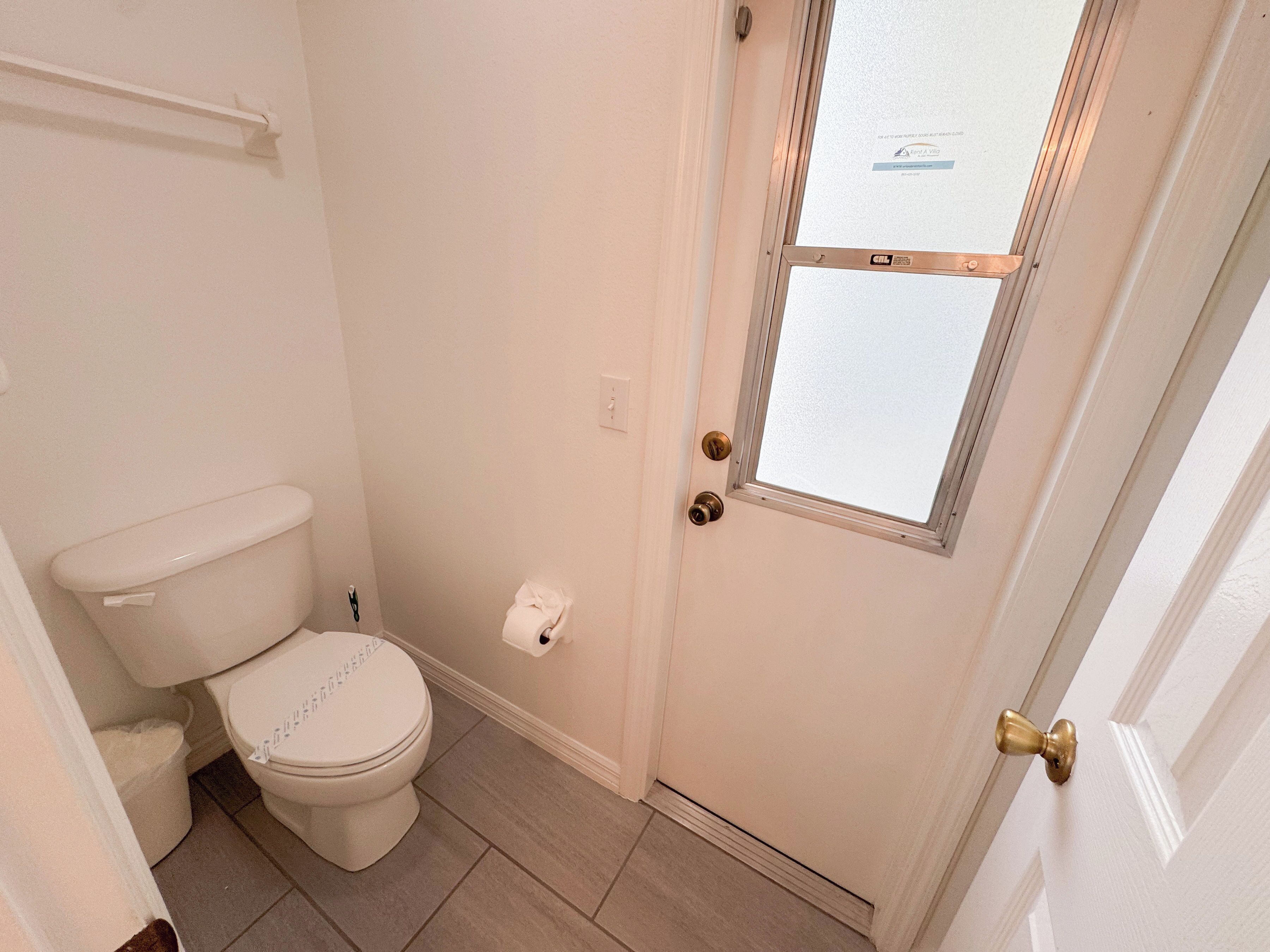 Un baño pequeño y limpio con inodoro, toallero y puerta con ventana.