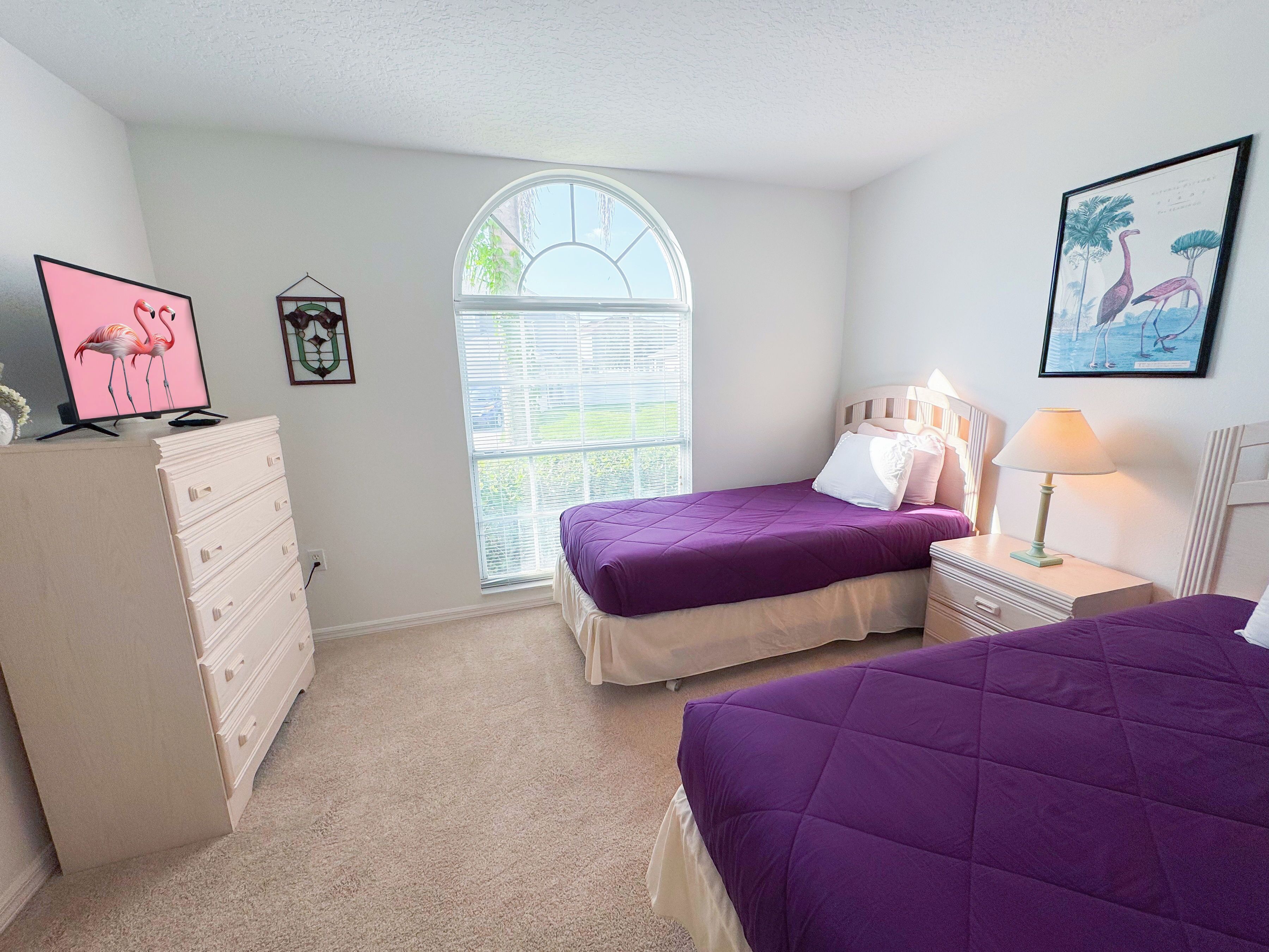 A bedroom with two beds, a dresser, a window with blinds, a lamp, and a framed picture on the wall.