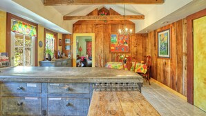 A rustic kitchen with wooden walls, a large island with drawers, and a dining area with a colorful tablecloth. - Charming Arroyo Cottage walking distance from Old Town Arroyo (Arroyo Grande)