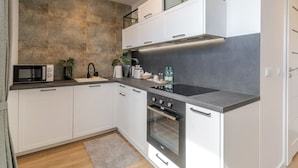 A modern kitchen with white cabinets, a black countertop, a built-in oven, and a backsplash with a textured pattern. - Chopina Comfort Studio (Katowice)
