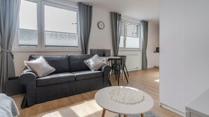 A modern living room with a grey sofa, a round coffee table, and a dining area with a small table and chairs. - Chopina Comfort Studio (Katowice)
