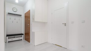 A modern, minimalist room with white walls, a wooden door, and a bench with storage drawers. - Francuska Comfort Apartment (Katowice)
