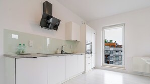 A modern kitchen with white cabinetry, a built-in oven, and a window overlooking a residential area. - Francuska Comfort Apartment (Katowice)