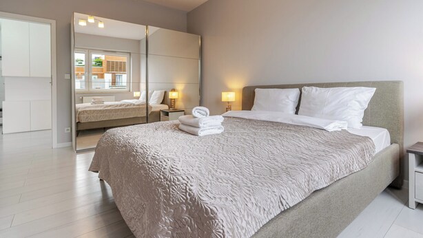 A modern bedroom with a large bed, a mirror, and bedside lamps. - Francuska Comfort Apartment (Katowice)