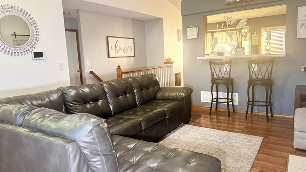A living room with a leather sofa, a white rug, and a kitchen area with bar stools. - Soothing 4-bedroom house with AC in charming Fountain (Fountain)