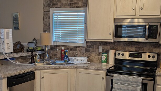 A modern kitchen with white cabinets, a stainless steel microwave, and an oven. - Lovely 4-bedroom mobile home in Oak Island 6 MIN WALK TO BEACH (Oak Island)