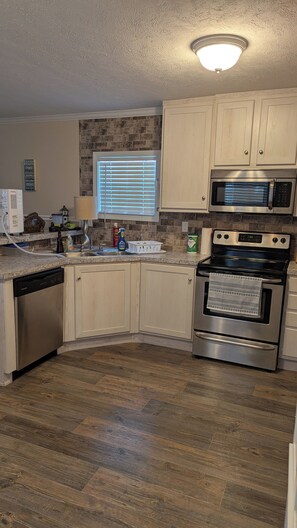 A modern kitchen with white cabinets, a stainless steel microwave, and an oven. - Lovely 4-bedroom mobile home in Oak Island 6 MIN WALK TO BEACH (Oak Island)