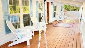 Une véranda couverte avec des fauteuils à bascule blancs et une balançoire.