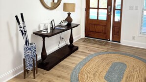 Une pièce avec un plancher en bois, un tapis rond, un miroir, une lampe et une porte avec des fenêtres.