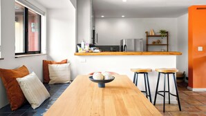 Une cuisine moderne dotée d’un plan de travail en bois, d’un réfrigérateur en acier inoxydable et d’un four encastré. On y trouve deux tabourets de bar et une table à manger en bois sur laquelle est posé un récipient contenant des objets décoratifs.