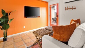 Un salon avec un mur orange, un téléviseur à écran plat, des meubles en osier et une plante en pot.