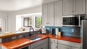 Une cuisine moderne avec des armoires blanches, un plan de travail rouge, un four à micro-ondes en acier inoxydable et un dosseret de carrelage disposé en motif chevrons.
